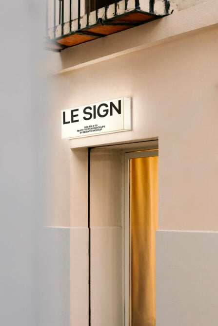 Lit horizontal sign on white wall above shop entrance glowing at night