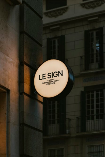 Lit cream circular storefront sign on dark stone building facade at dusk