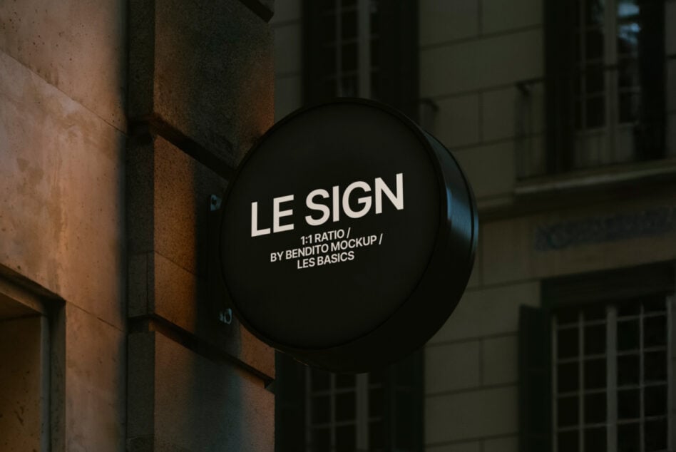 Black illuminated round sign on textured stone wall with building windows behind