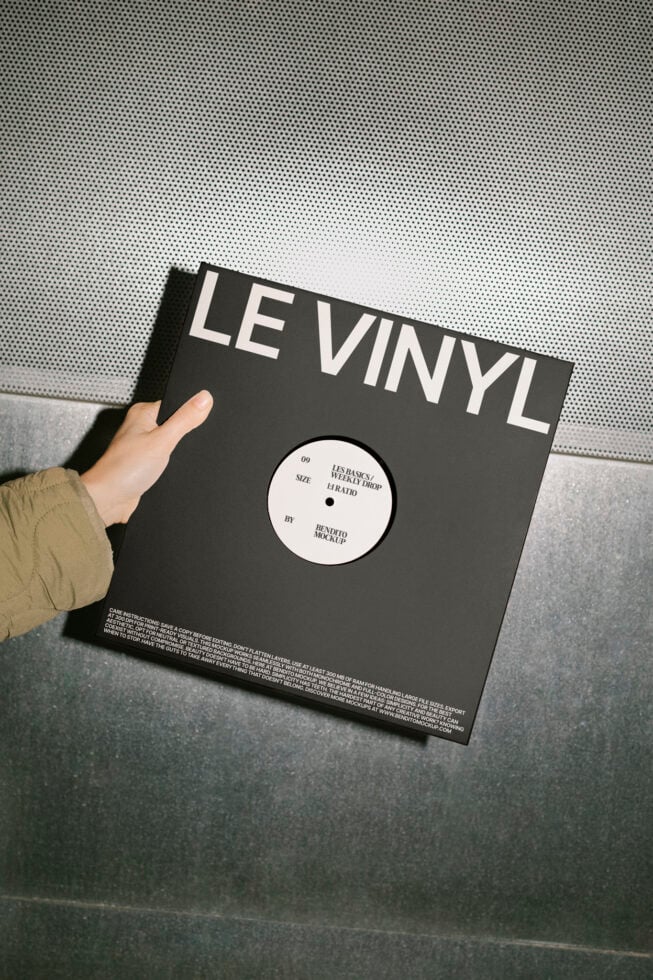 Hand holding black vinyl record mockup with bold white typography Le Vinyl on the cover against a metallic surface. Perfect for designers and branding.