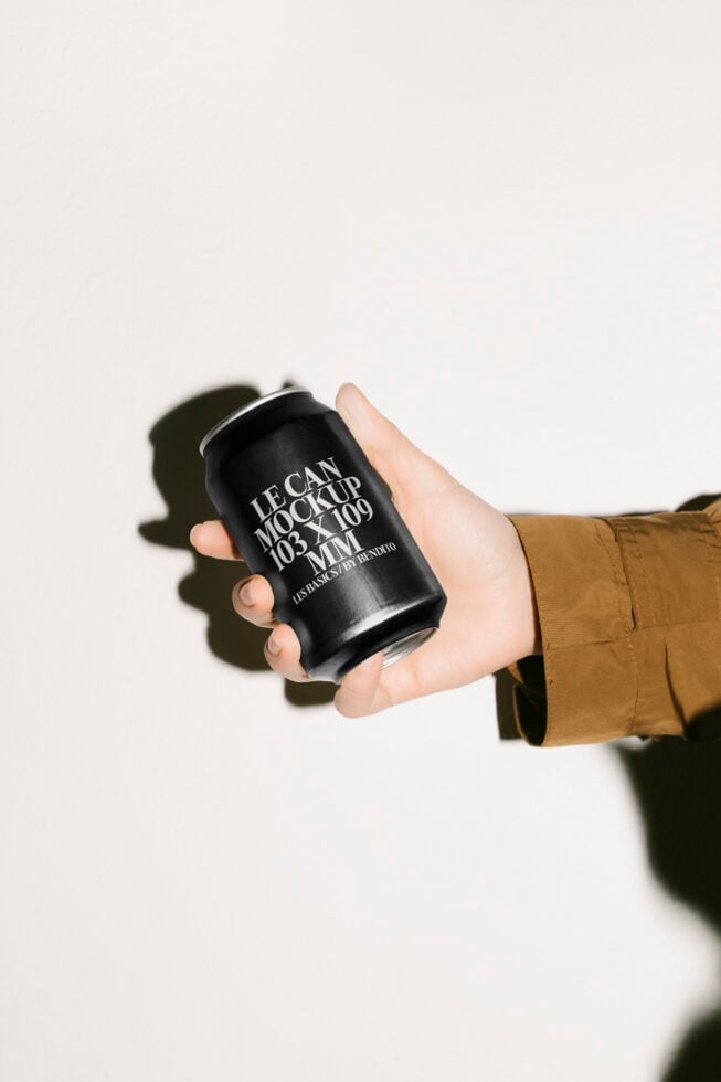 Hand holding black can mockup with customizable design leaning against a light background ideal for product branding showcasing marketing presentations
