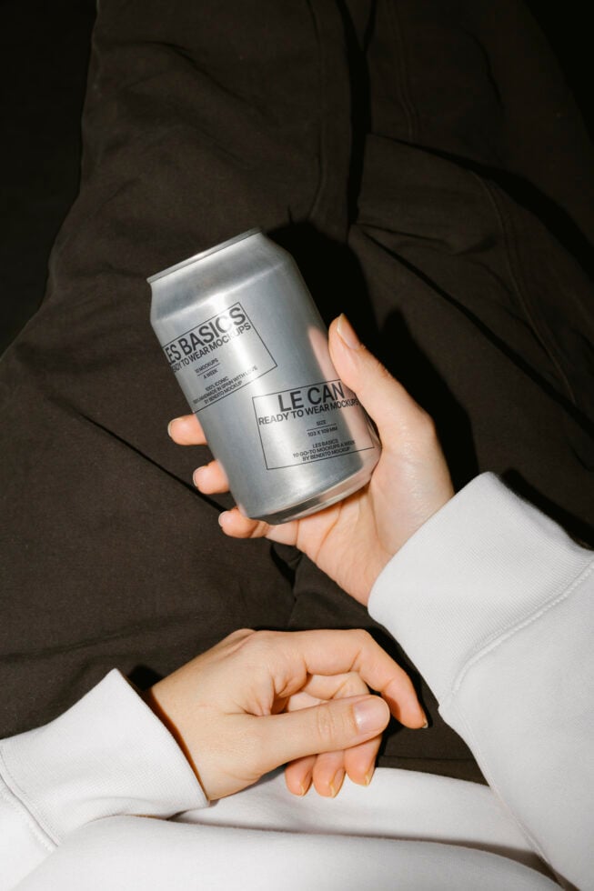 Person holding a silver soda can mockup in casual attire. Perfect for showcasing branding designs. Keywords: mockup template product graphic designers.