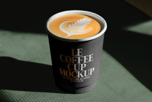 Coffee cup mockup with latte art design on dark green surface. Ideal for showcasing brand designs. Keywords: coffee cup, mockup, latte art, design asset.
