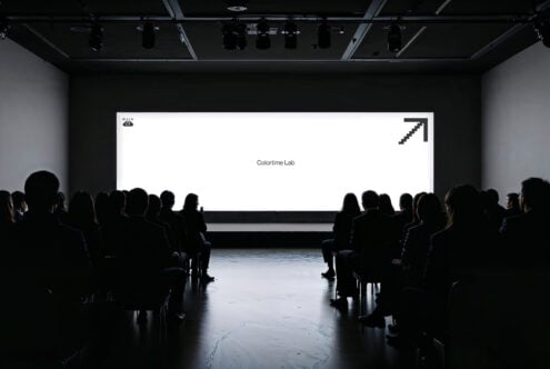 Audience watching a presentation in a dark room with a large glowing screen displaying Colortime Lab perfect for designers seeking inspiration mockup template