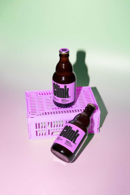 Two brown glass bottles with pink labels on a pastel crate against a green backdrop. Beverage mockup for designers showcasing modern label design.
