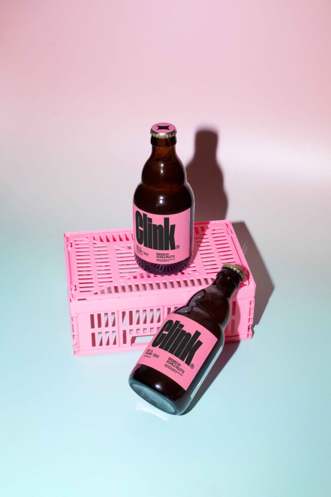 Two brown glass bottles with bold pink labels and caps on a pink crate against a pink gradient backdrop, ideal for product mockup design templates.
