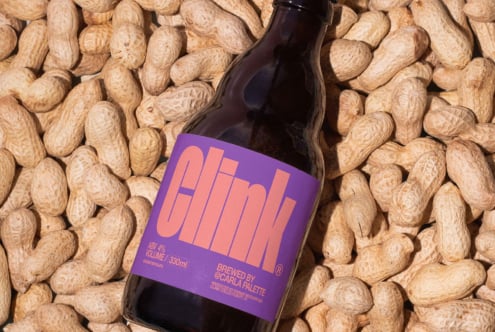 Beer bottle with purple label on scattered peanuts, showcasing product mockup design for beverage branding. Perfect for graphic designers seeking inspiration.