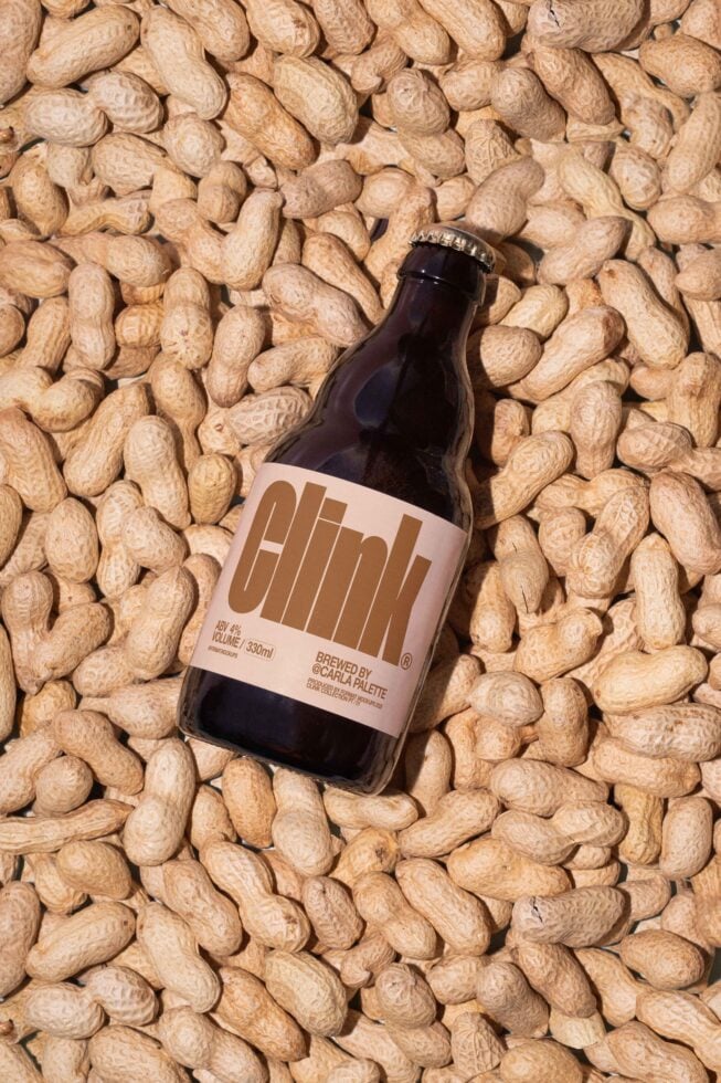 Beer bottle with minimalist label design laying on scattered peanuts. Perfect for mockups, branding, product presentation. Ideal for designers.