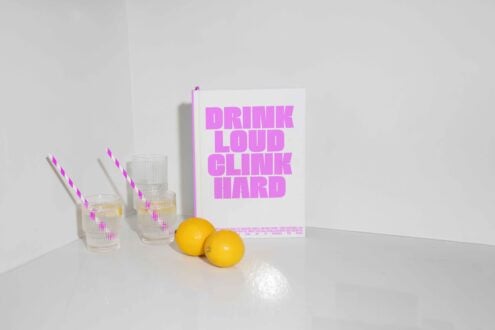 Minimalist drink mockup featuring a book titled DRINK LOUD CLINK HARD, glassware with striped straws, and lemons. Perfect for creative graphic designs.