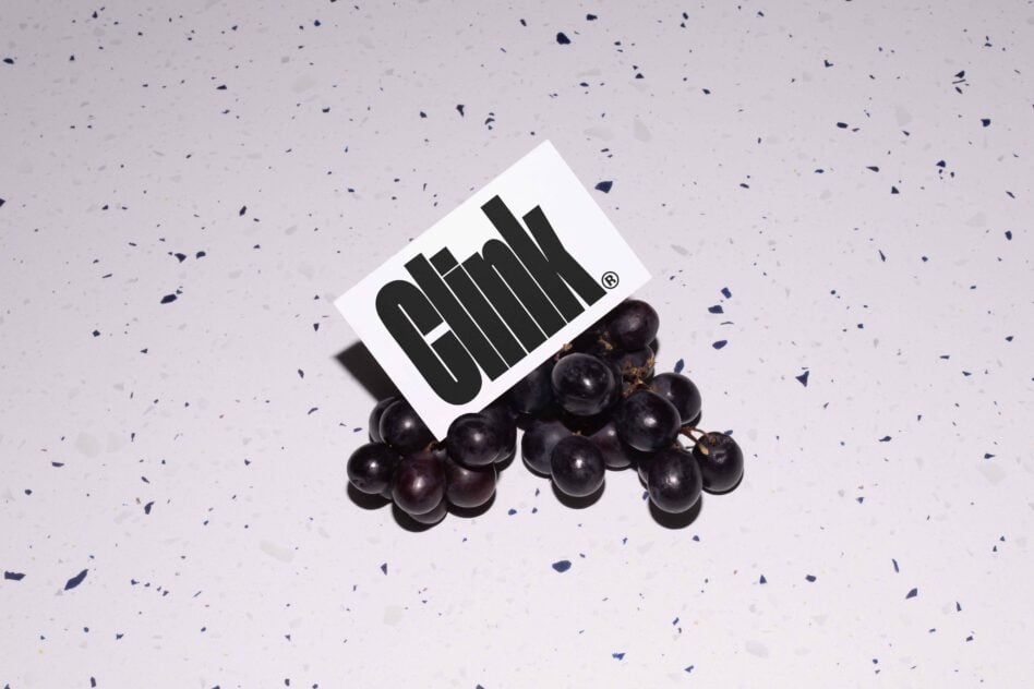 White card with black text tilted on pile of grapes on light purple ground
