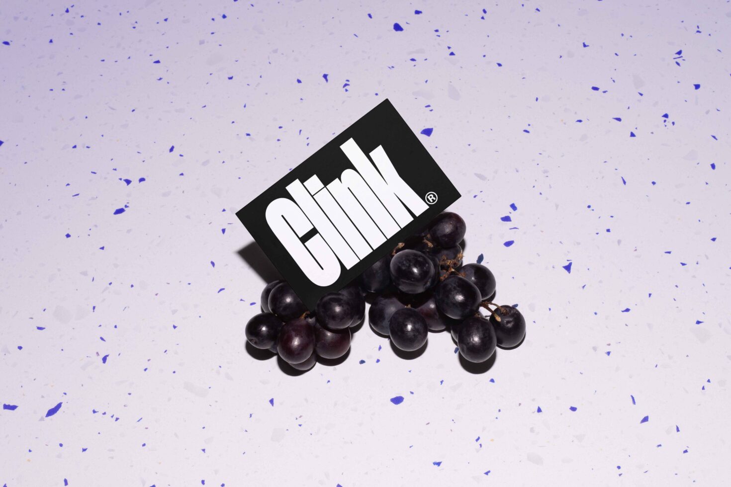 Mockup featuring a black card with bold white text nestled on grapes against a speckled purple background. Ideal for design presentations and templates.