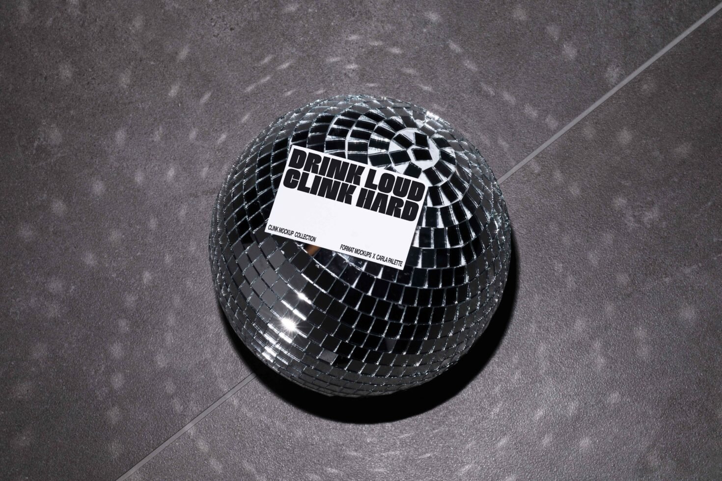 Mockup of a reflective disco ball on a dark surface featuring bold typography text Drink Loud Clink Hard offering a modern graphic design asset.