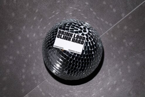 Mockup of a reflective disco ball on a dark surface featuring bold typography text Drink Loud Clink Hard offering a modern graphic design asset.