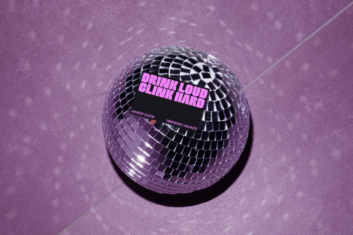 Mockup featuring a disco ball with a card displaying the phrase Drink Loud Clink Hard on a purple surface. Ideal for graphic design and templates.