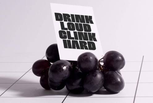 Modern typography design on card with bold text Drink Loud Clink Hard displayed on bunch of grapes. Perfect for branding mockups graphics design templates