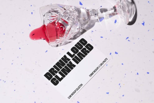 Crystal glass on side with red liquid spilling on speckled surface. Nearby is a card with bold text Drink Loud Clink Hard. Ideal for template mockups.