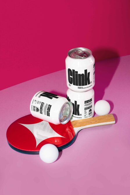 Ping pong setup with three white soda cans labeled Clink on a pink background. Ideal for branding mockup, graphic design, and product presentation.