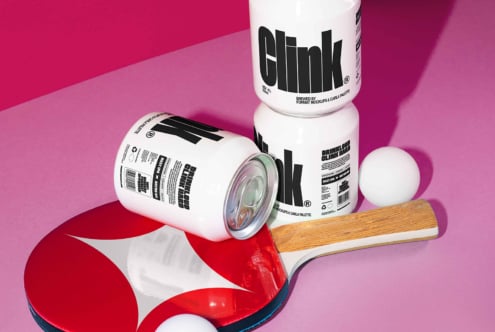 Three cans labeled Clink on a vibrant pink backdrop with a ping pong paddle and balls Mockup design vibrant packaging SEO keywords digital assets