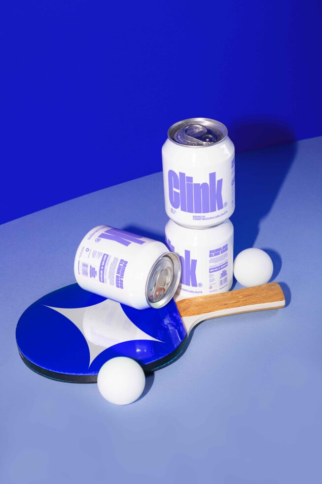 Cans with bold typography on a blue table with a ping pong paddle and balls mockup. Perfect for graphic design and beverage packaging templates.