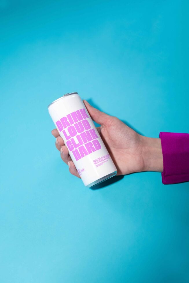 Hand holds sleek can with bold pink text against blue background ideal for mockups templates vibrant packaging design digital assets for designers.
