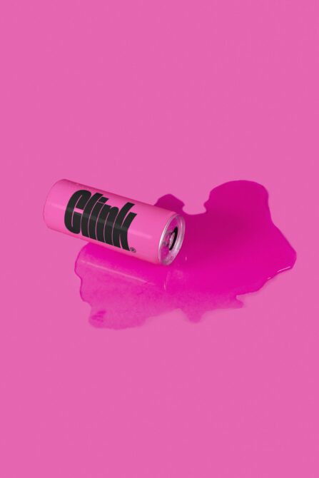 Hot pink beverage can with black horizontal lines on magenta background puddle