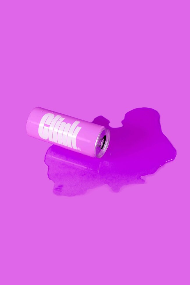 Pink beverage can with white horizontal lines on magenta background puddle