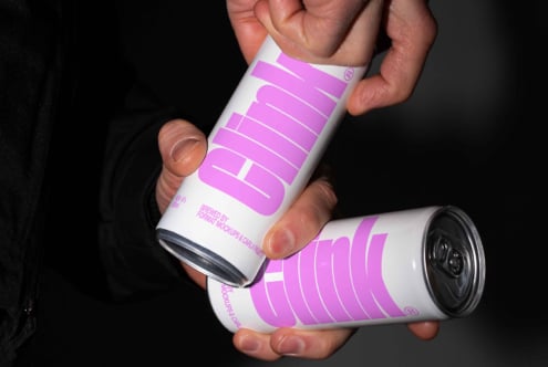 Mockup of hands holding two beverage cans with bold pink logo clink on a dark background suitable for digital design assets branding and packaging.