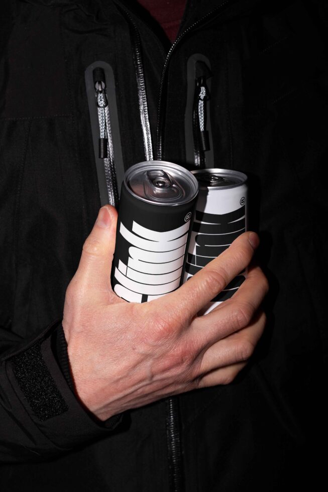 Hand holding black and white beverage cans in a zipped jacket. Minimalist drink mockup design. Ideal for designers creating product packaging templates.