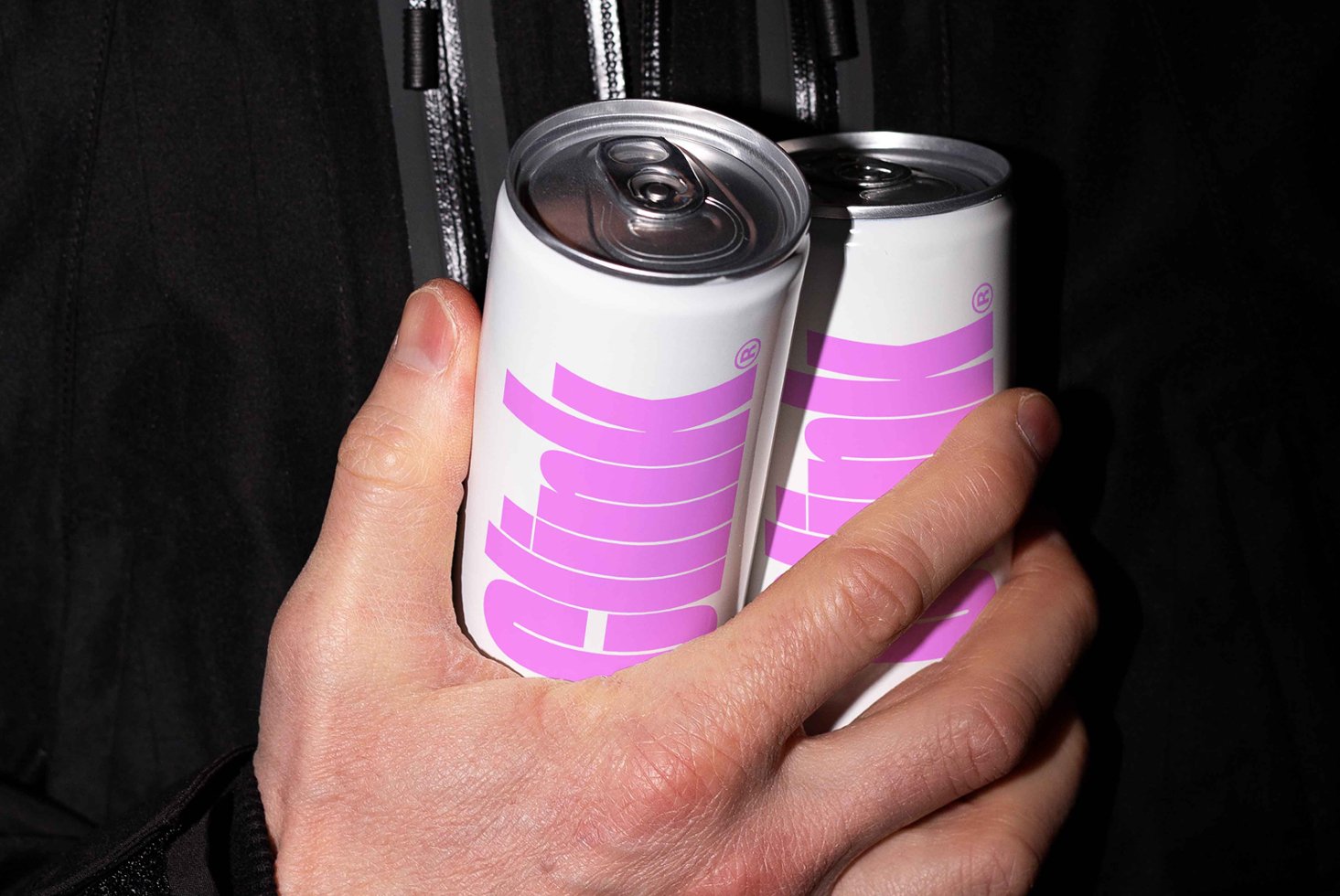 Person holding two sleek soda cans with purple branding on white background. Ideal for product mockups, packaging design templates, digital graphics.