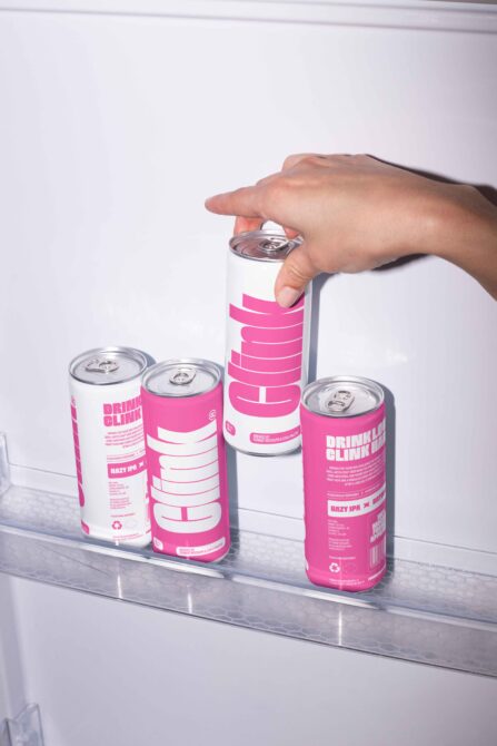 Hand holding a white and pink energy drink can in a fridge mockup, surrounded by similar cans, ideal for graphic design and branding projects.
