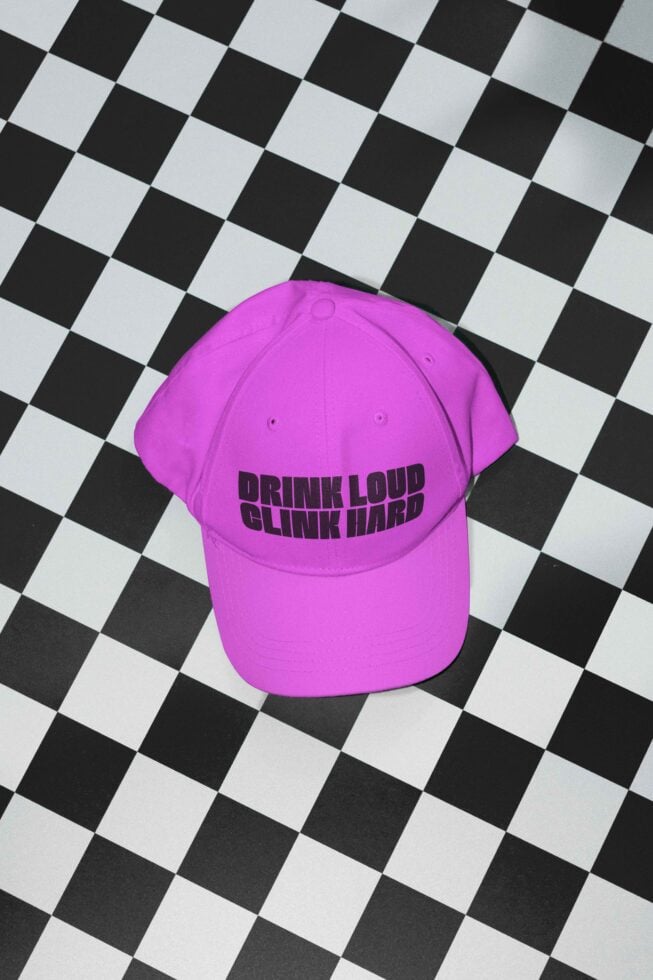 Purple cap with Drink Loud Clink Hard text placed on black and white checkered background. Ideal for mockup showcases, graphic design projects, trendy.