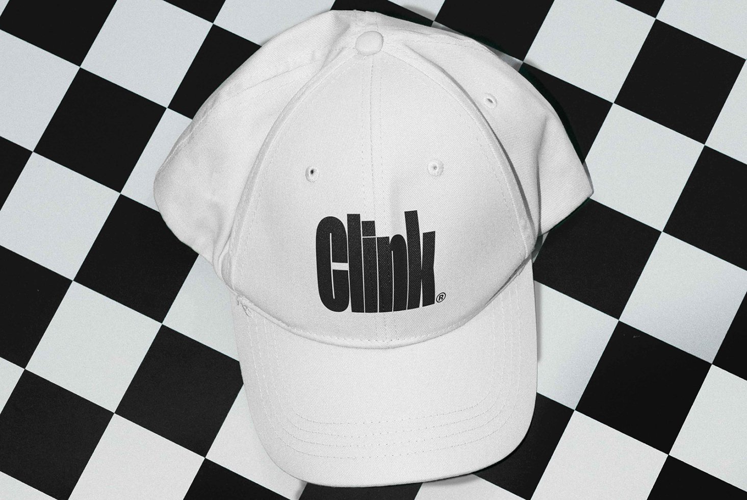 White baseball cap with bold black Clink logo placed on a black and white checkered surface. Ideal for branding mockups and merchandising design.