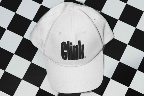 White baseball cap with bold black Clink logo placed on a black and white checkered surface. Ideal for branding mockups and merchandising design.