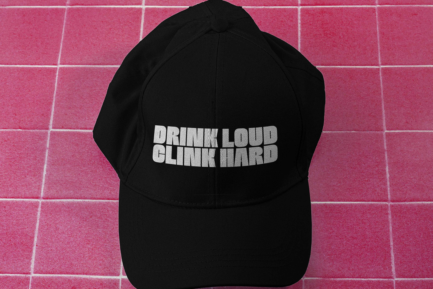 Black baseball cap with white text on pink tile surface overhead view