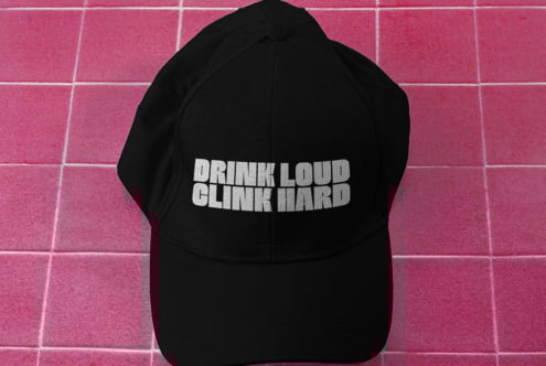 Black baseball cap mockup on a pink tiled background featuring bold white text Drink Loud Clink Hard ideal for designers fashion templates branding