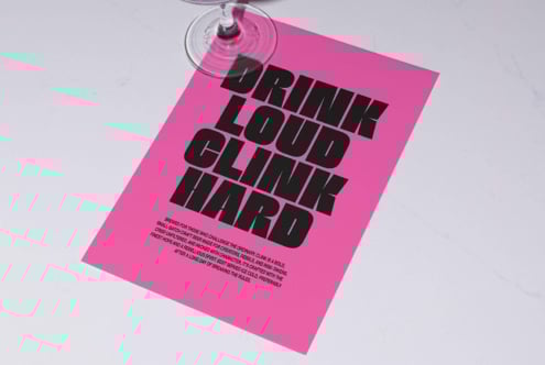 Pink flyer mockup with bold black text Drink Loud Clink Hard by a wine glass on a marble surface graphic design template typography SEO designers asset