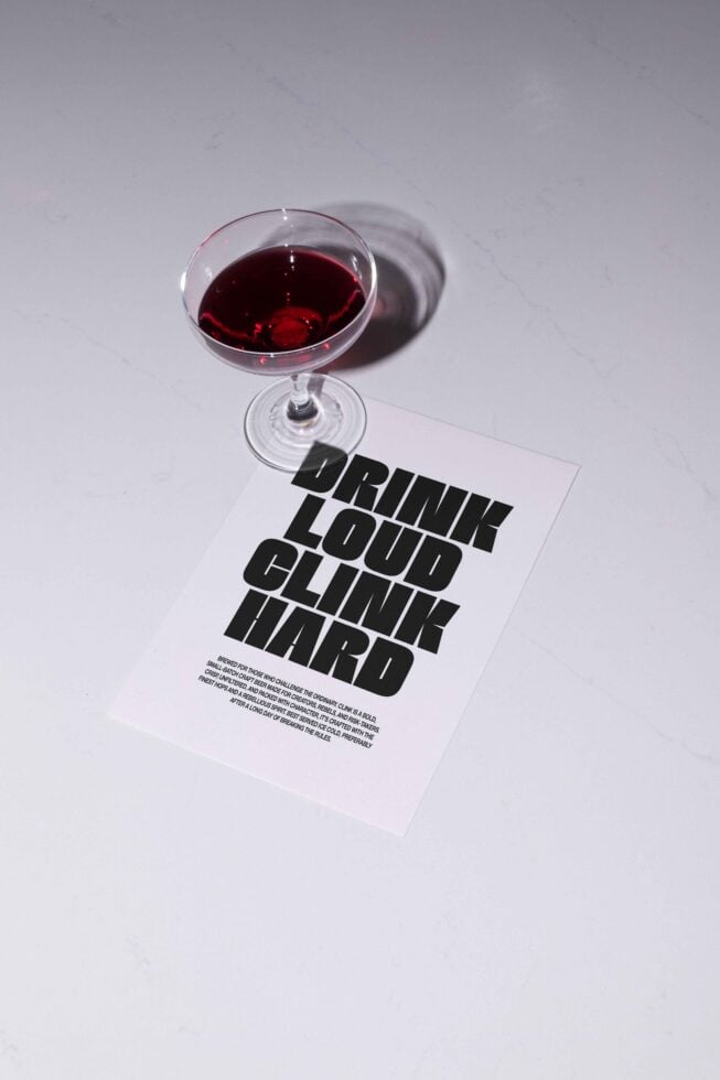 Cocktail glass on white surface with bold typography mockup saying Drink Loud Clink Hard. Ideal for graphic designers and typography projects.