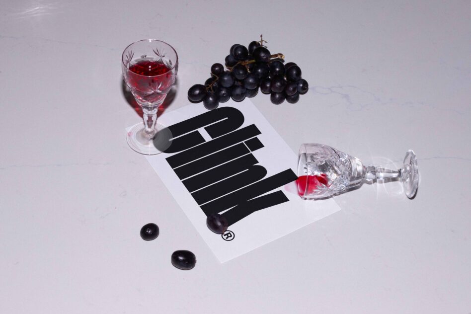 Wine glass with red liquid, black grapes, spilled wine on paper with bold text layout