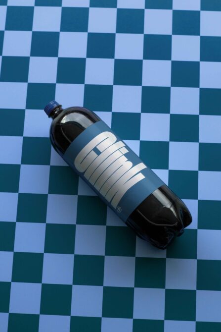 Plastic soda bottle with custom blue label placed on a blue white checkered surface mockup design branding packaging template for designers.