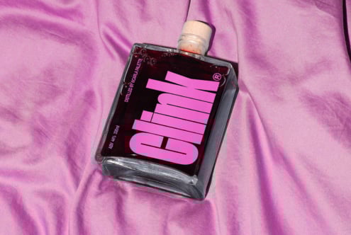 Glass bottle with bold pink typography on purple fabric background ideal for mockups templates packaging design branding resources digital assets.