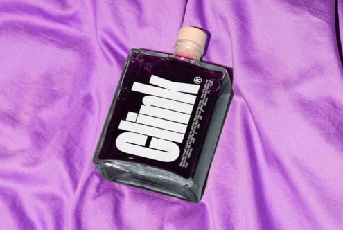 Glass bottle with bold typography label on purple fabric background. Ideal for mockups and graphic design projects. High-quality designer asset.