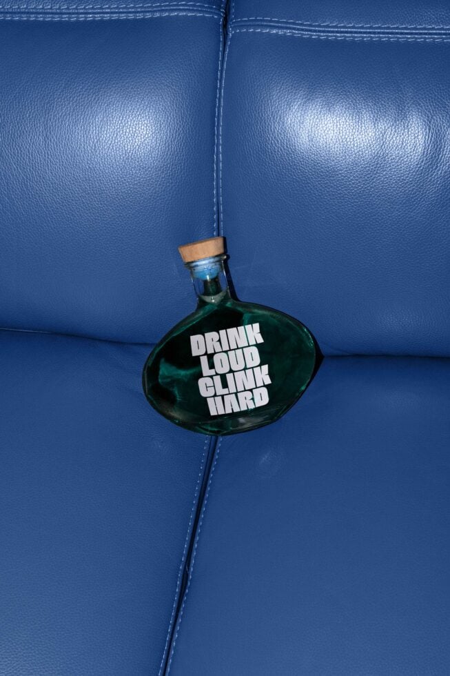 Bottle with text Drink Loud Clink Hard on a blue leather surface, ideal for graphic design and branding projects. Keywords: mockups, design, template, bottle.