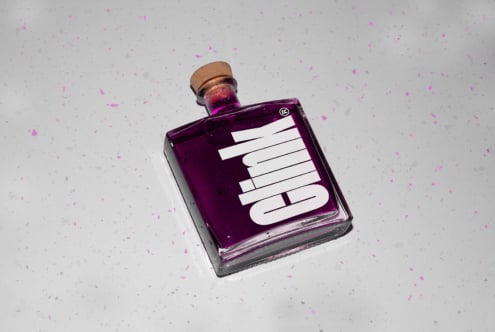 Purple liquid in a square glass bottle with a cork on a speckled gray surface. Suitable for graphic design mockups and product display templates.