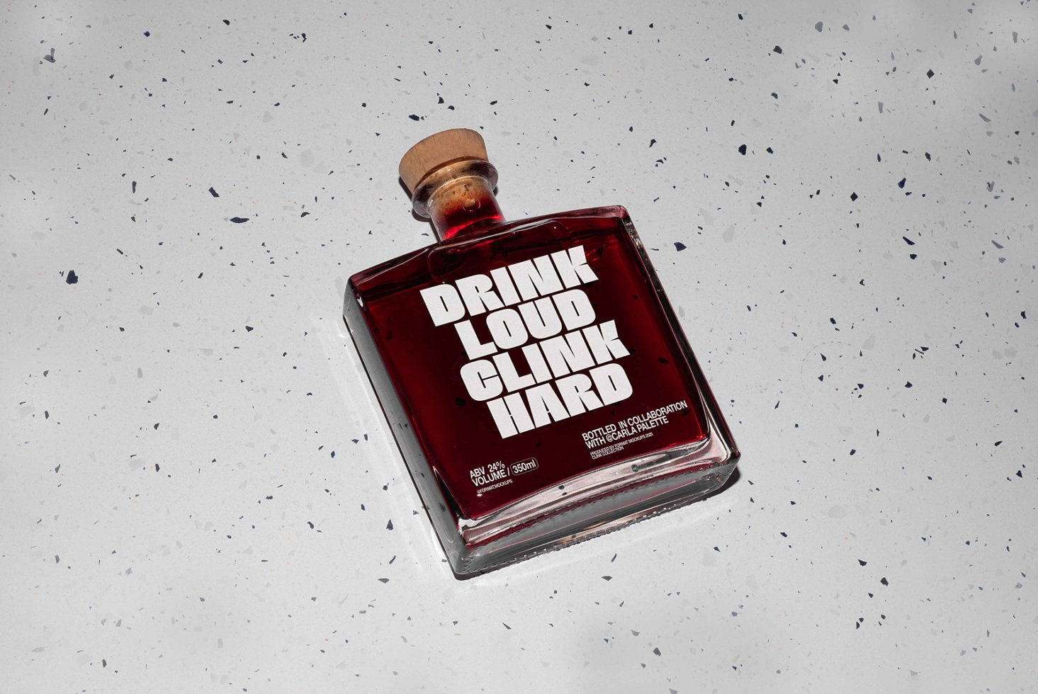 Glass bottle with bold typography Drink Loud Clink Hard on speckled surface. Ideal for designers seeking graphics or packaging mockups.
