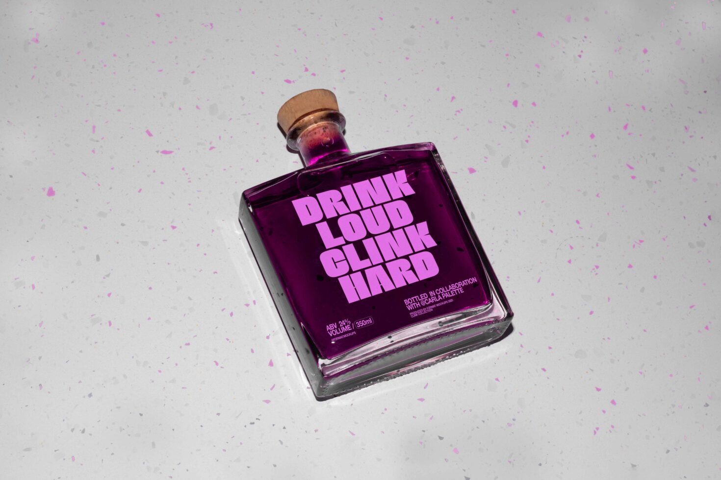 Purple glass bottle with bold pink typography text Drink Loud Clink Hard on speckled surface perfect for designers looking for unique mockup graphics.
