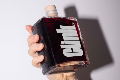 Hand holding a square glass bottle with bold typography label clink and wooden cork. Ideal for packaging mockup templates digital assets designers.