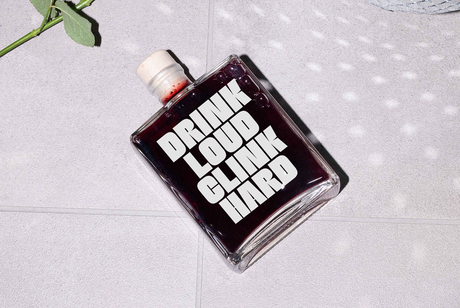 Flat square bottle with bold white text Drink Loud Clink Hard on dark liquid. Minimalist design, perfect for typography mockups or graphic projects.