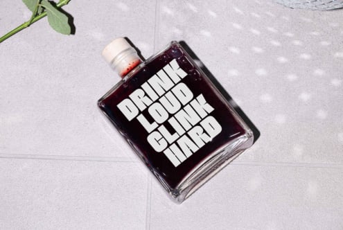 Flat square bottle with bold white text Drink Loud Clink Hard on dark liquid. Minimalist design, perfect for typography mockups or graphic projects.