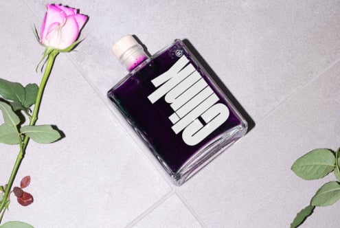 Flatlay of a tilted purple ink bottle with bold typography on a gray tile surface next to a pink rose Digital assets Marketplace Mockup Graphics
