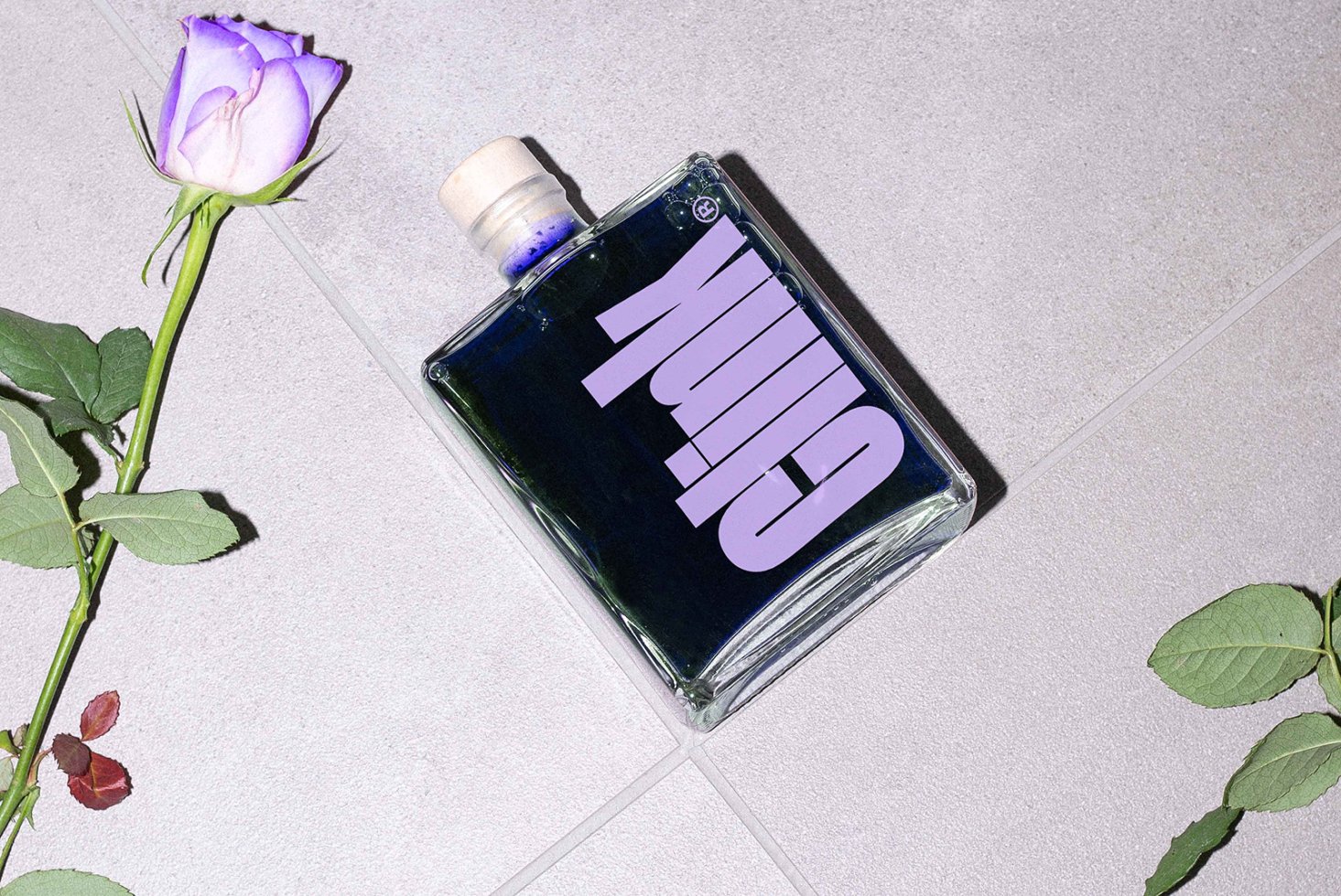 Flat lay of a bold text bottle design with violet ink, accompanied by a purple rose on a gray concrete background. Perfect for design mockups.